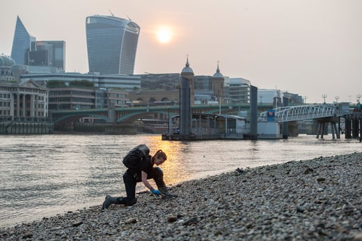 Mudlark Monika Buttling-Smith kneels on a rocky shore, collecting objects © London Museum